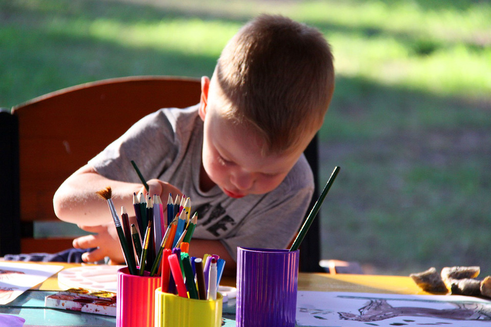 En pojke sitter vid ett bord utomhus och ritar.