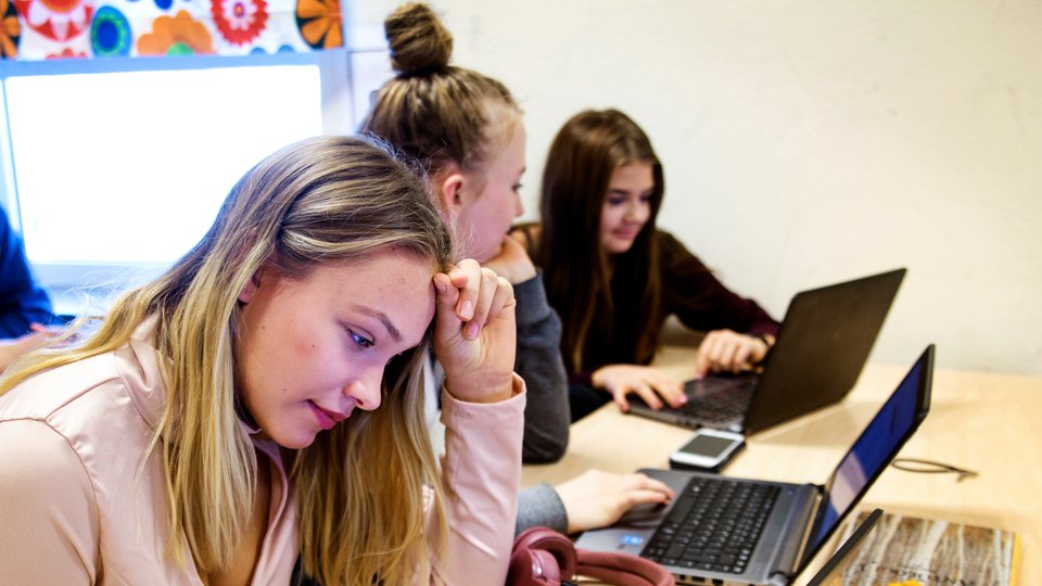 Elever som sitter i skolbänkar med bärbara datorer.