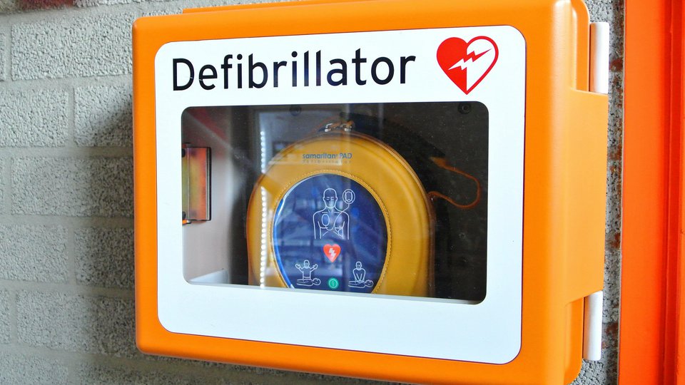En orange defibrillator monterad på en betongvägg.