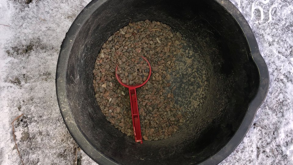En svart hink med sand och en röd liten spade att ösa med.