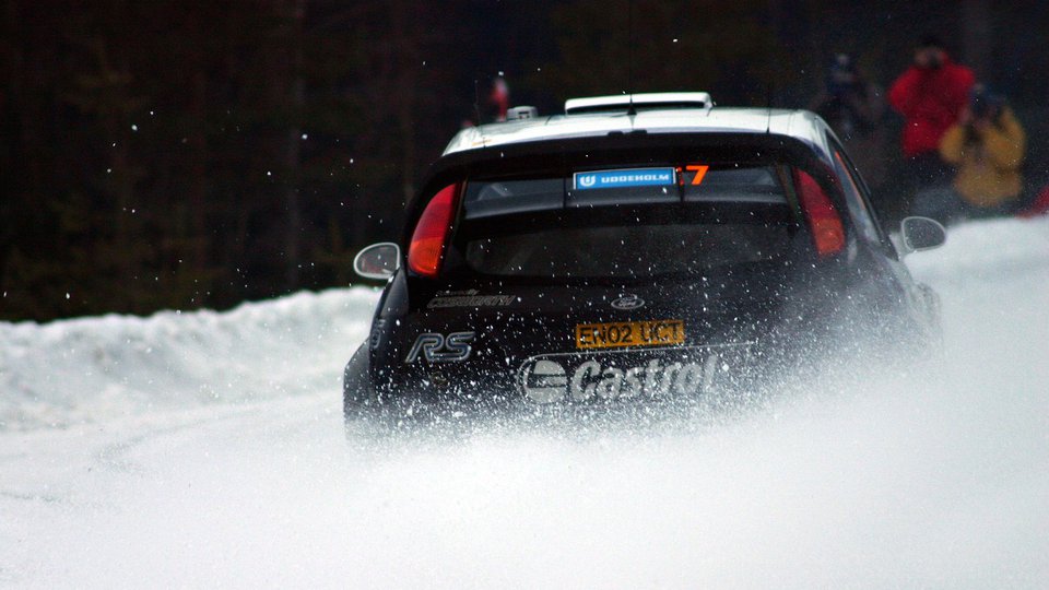 Mörkfärgad rallybil sladdar i snö.