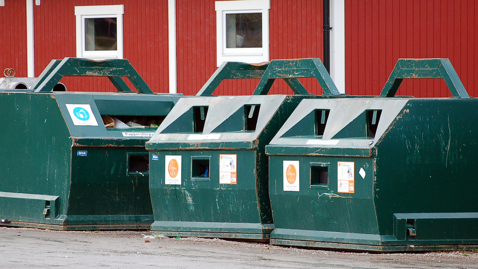 Containrar för återvinning står framför en röd byggnad