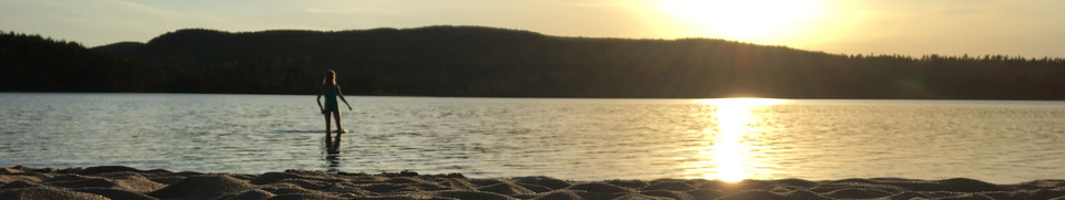Ett barn står i vattnet i en sjö med kvällssol. 