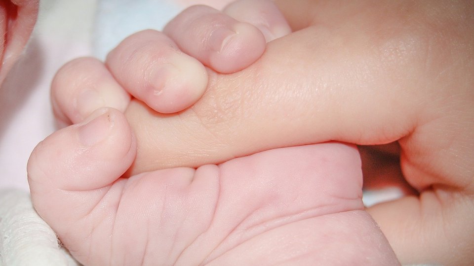 Ett spädbarn håller i en vuxens finger.