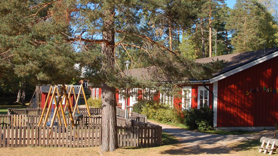 En röd byggnad med lekplats bland tallar i Strömsbruk.