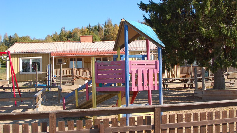 En gul träbyggnad med en lekplats i förgrunden.