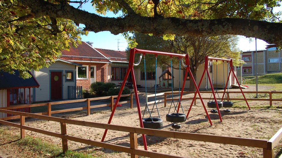 Trä- och tegelbyggnad, lekplats med gungor.