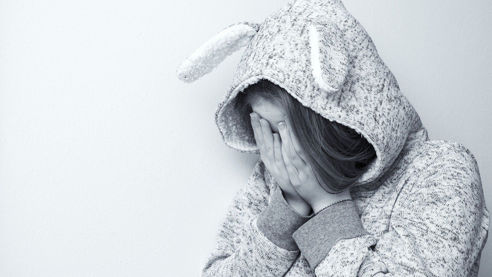 Flicka med huvtröja med kaninöron gömmer ansiktet i händerna