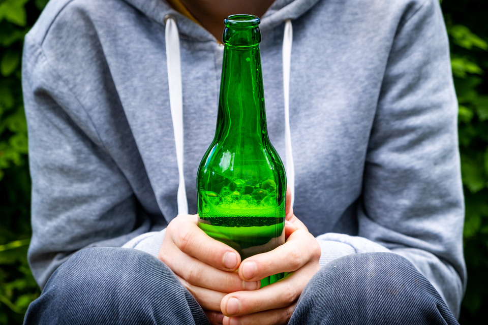 En ung person håller i en ölflaska.