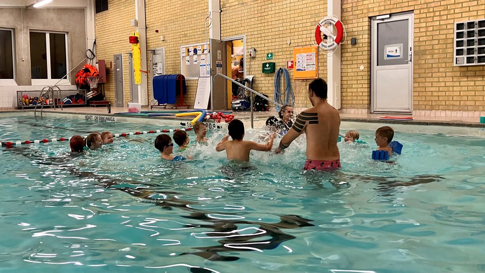 Barn som plaskar i en simbassäng tillsammans med en vuxen person.