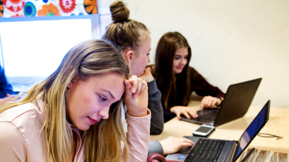 Tre flickor i grundskoleålder sitter och jobbar vid sina bärbara datorer
