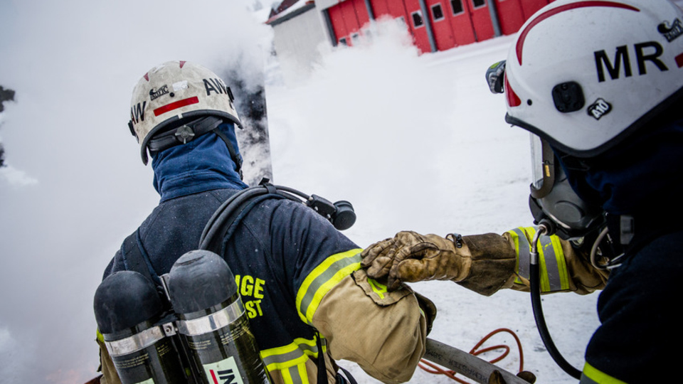 Två brandmän med rökdyningsutrustning bekämpar en brand.