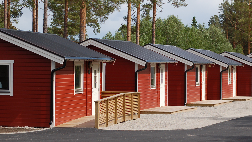 Sex röda gäststugor på rad med tallar i bakgrunden, Sörfjärdens camping, Gnarp