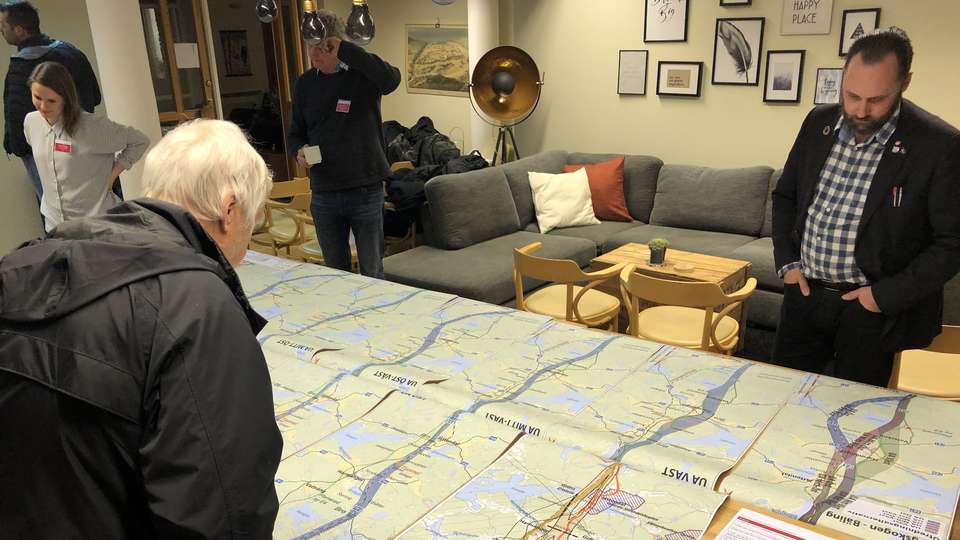 Två män tittar på kartor utlagda på ett stort bord.