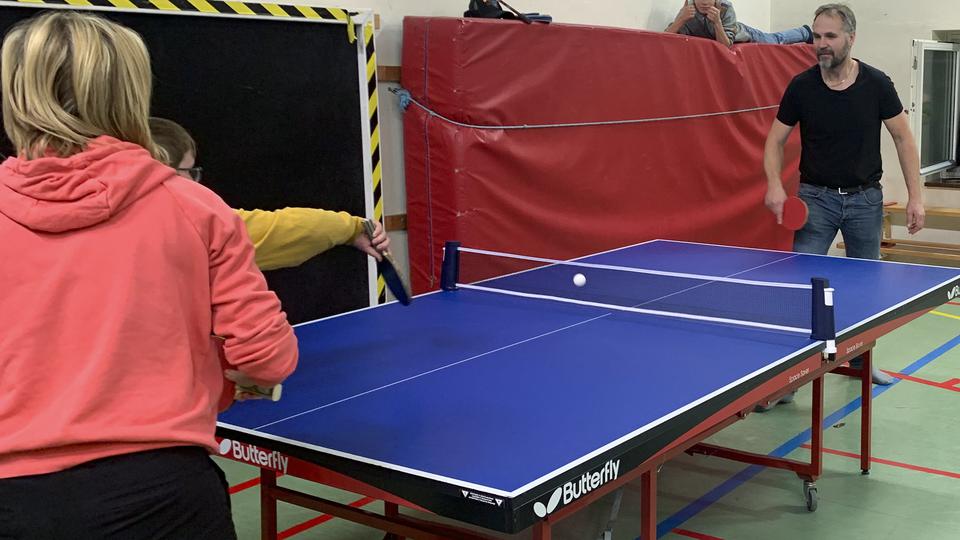 Några personer spelar bordtennis i en gymnastiksal.