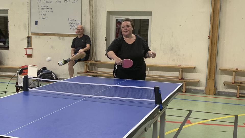 En kvinna spelar pingis i en gymnastiksal.