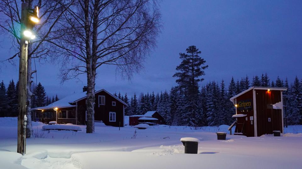 Vinterkväll med snö och några röda byggnader.