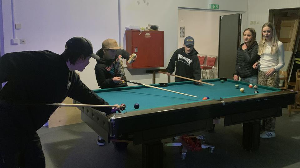 Ungdomar spelar biljard och några tittar på.