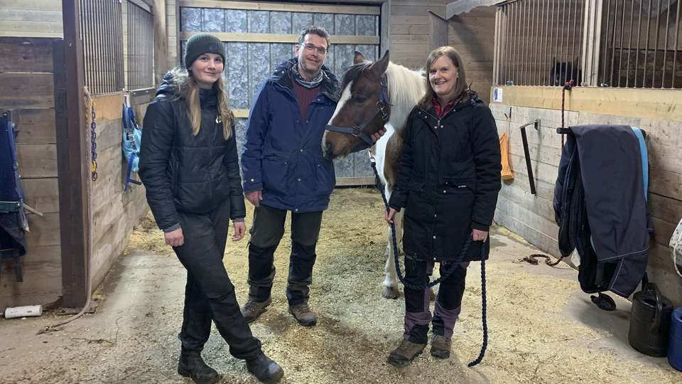 Tre personer står i ett stall tillsammans med en häst.