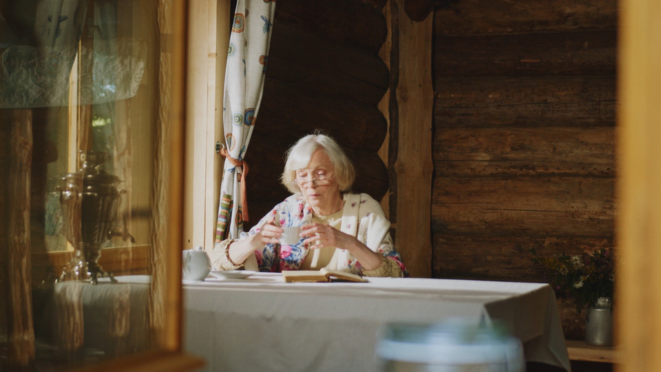 Äldre kvinna sitter ensam vid ett köksbord.