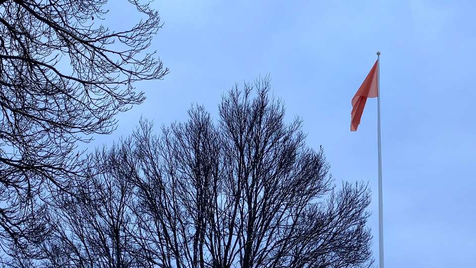 Hissad orange flagga mot en molnig himmel.