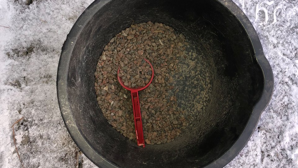 En svart hink med sand och en röd liten spade att ösa med.