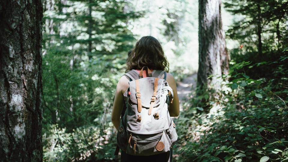 Kvinna med ryggsäck på stig i skog.