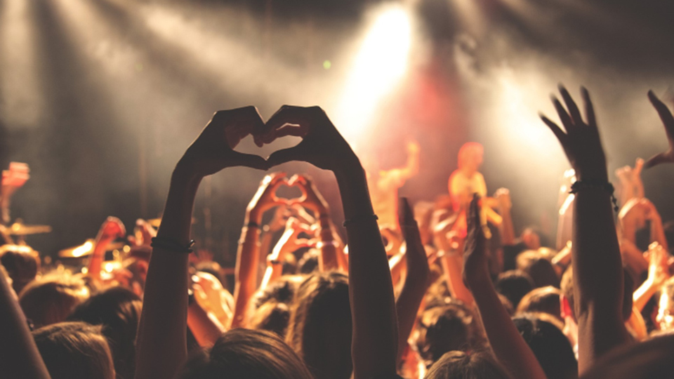 Uppsträckta händer som bildar ett hjärta i en folksamling vid konsert.