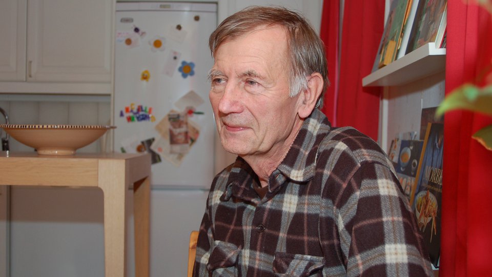 En äldre man sitter i sitt kök.