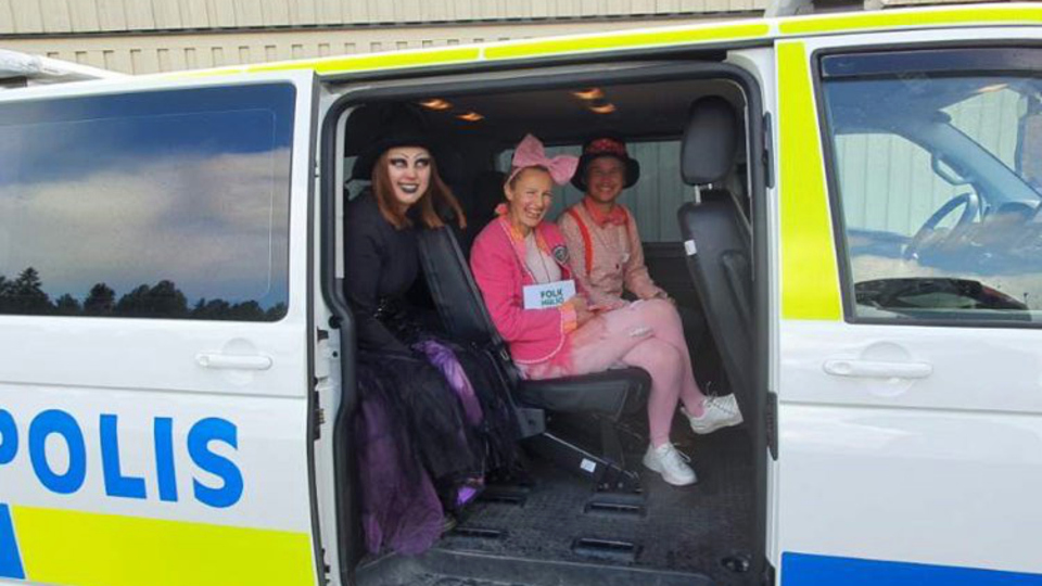 Tre personer utklädda till sagofigurer sitter i baksätet i en polisbuss.