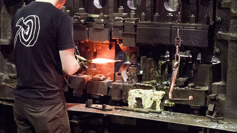 En smed smider en bit glödande stål i en maskin.