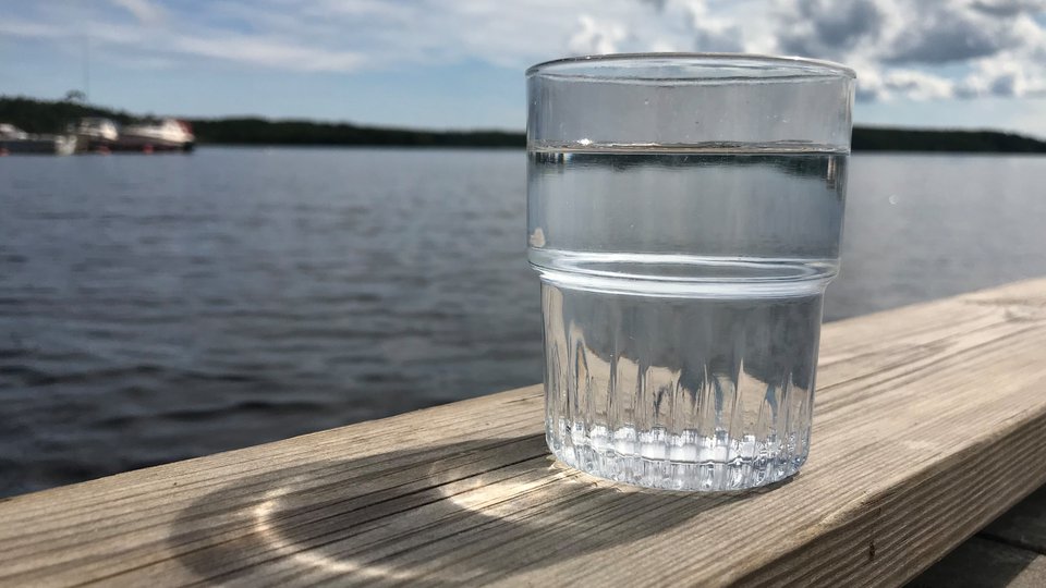 Ett glas vatten på ett räcke intill en havsvik.