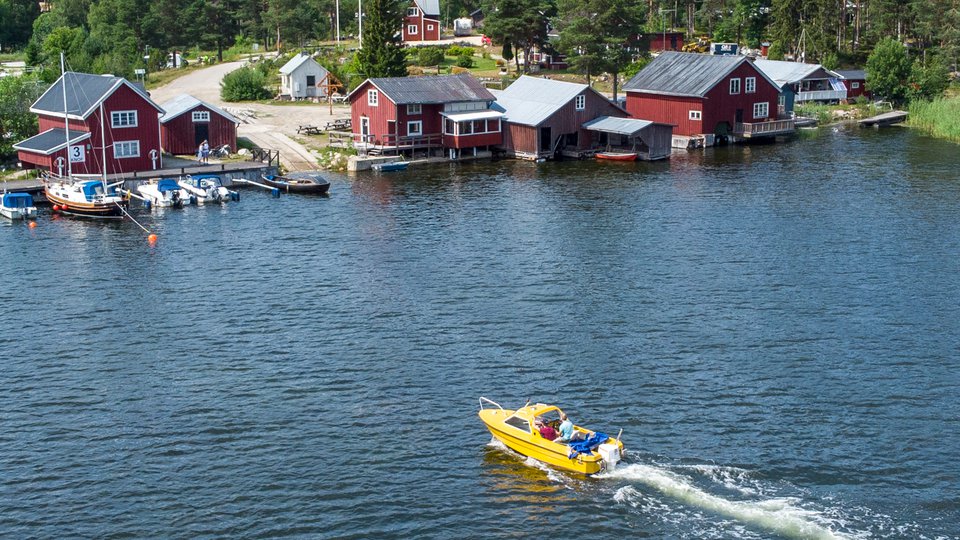 En gul båt som åker in mot bryggor vid röda sjöbodar.