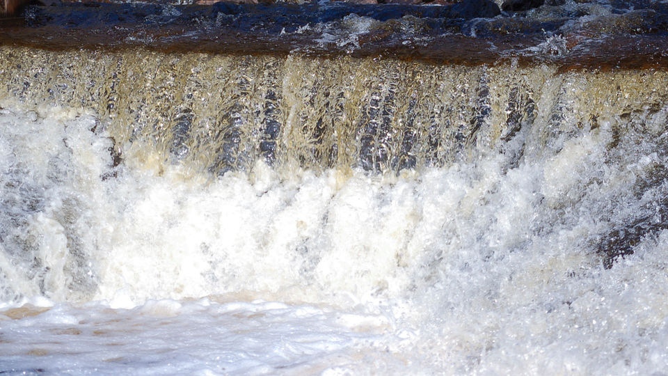 Bilden visar häftigt strömmande vatten över en åtröskel.
