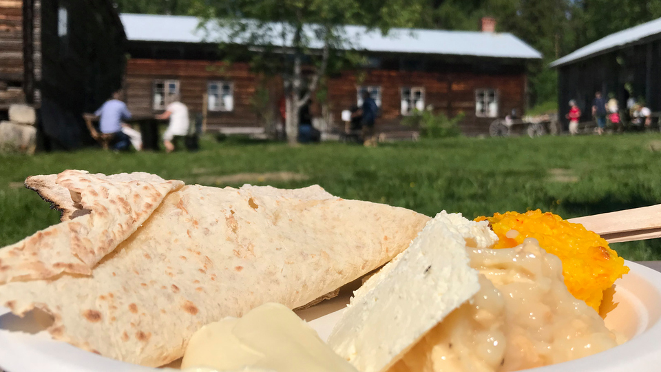 Bilden visar mat och bröd på en tallrik och i bakgrunden syns en gammal gård.