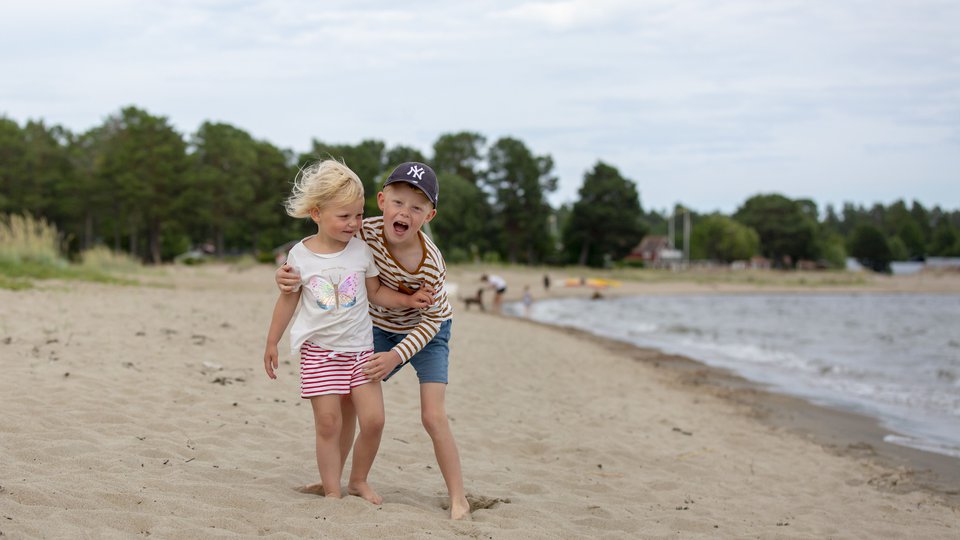 En liten flicka och en liten pojke i sommarkläder på en sandstrand.