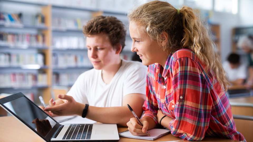 Två ungdomar sitter vid en laptop och studerar.