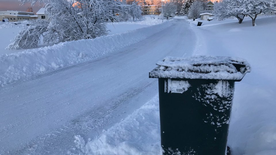 Bilden visar en framtagen soptunna vid en snöig väg.
