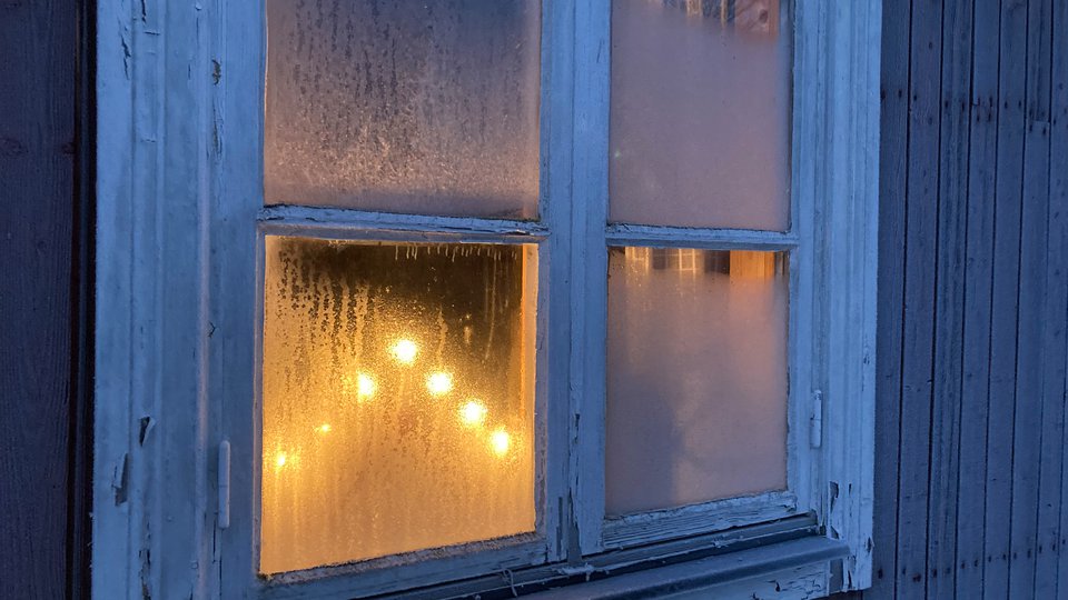 Bilden visar ett fönster med rimfrost och innanför lyser en adventsljusstake.