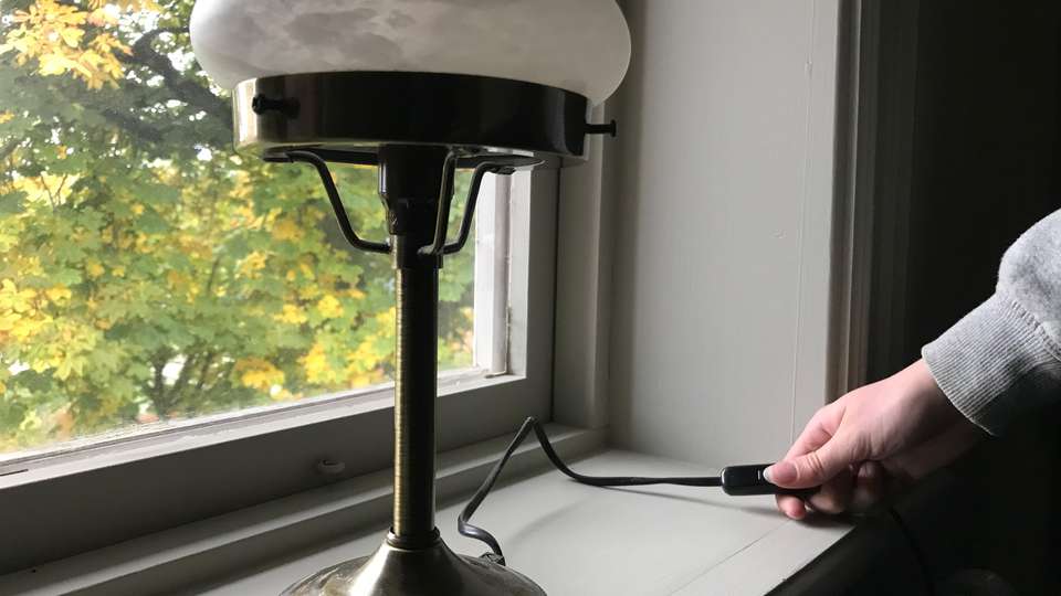 En person släcker en lampa som står i ett fönster.