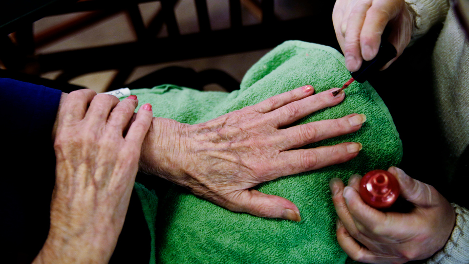 En äldre kvinna får sina fingernaglar målade.