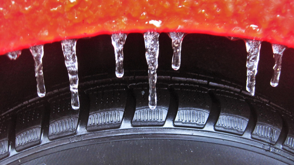 Närbild på ett däck och istappar som hänger från skärmkanten på en röd bil.