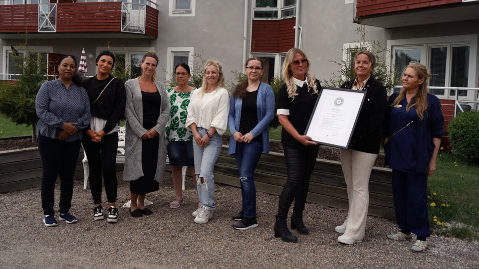 Nio kvinnor står framför en byggnad. En av dem håller upp ett diplom.