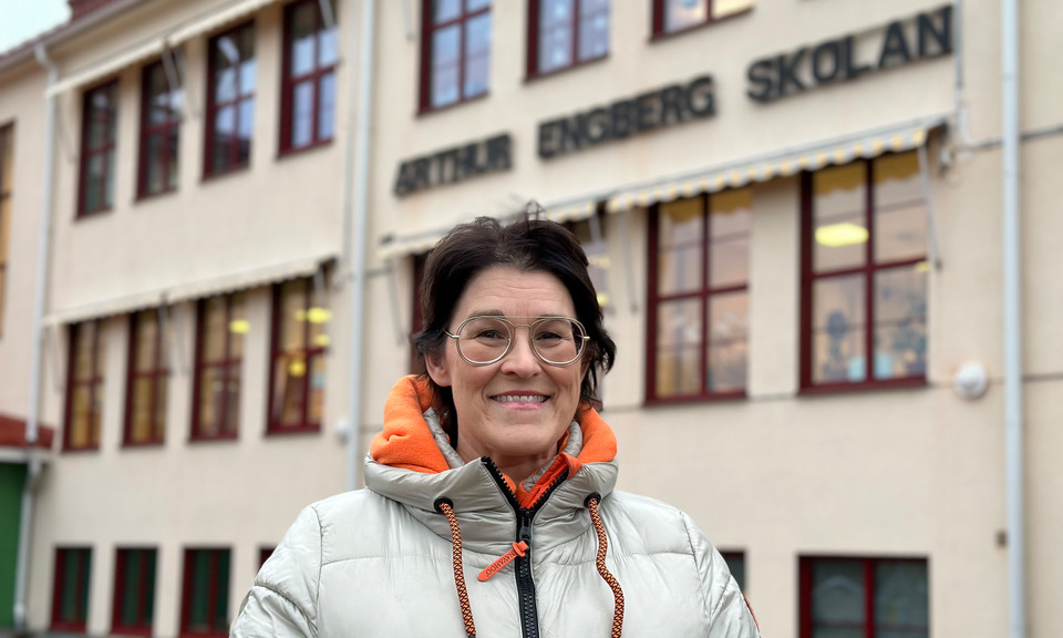 En kvinna i täckjacka står framför en skolbyggnad.