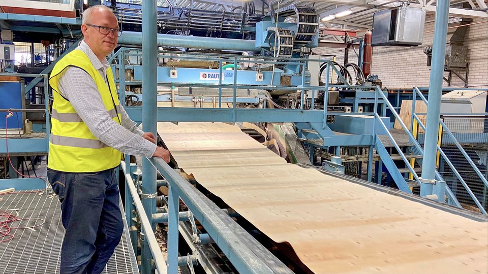 En man i varselväst står på en plattform och övervakar produktionen av fanér i en plywoodfabrik.