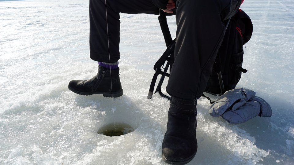 Ett par fötter intill ett hål i isen.