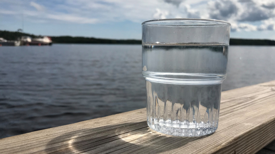 Ett glas med vatten på ett träbord med en havsvik i bakgrunden